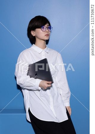 A young woman wearing glasses photographed against a blue background A young woman wearing glasses photographed against a blue background 111730672