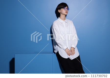 A young woman wearing glasses photographed against a blue background 111730702