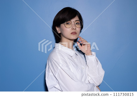 藍色背景下拍攝的一位戴眼鏡的年輕女子 藍色背景下拍攝的一位戴眼鏡的年輕女子 111730815