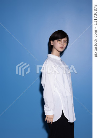 A young woman wearing glasses photographed against a blue background 111730878