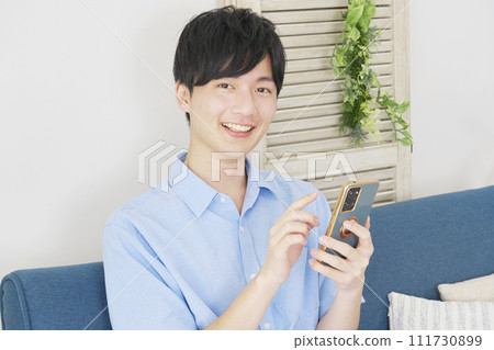 Man using smartphone in living room, looking at camera Man using smartphone in living room, looking at camera 111730899