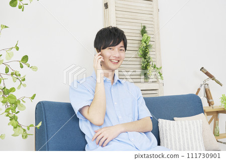 A man calling on a smartphone in the living room, looking at the camera A man calling on a smartphone in the living room, looking at the camera 111730901