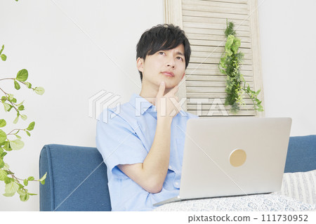 A man using a laptop while thinking in the living room A man using a laptop while thinking in the living room 111730952