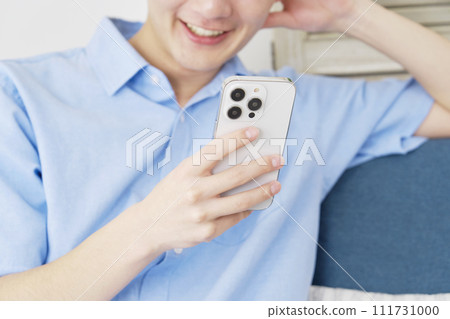 Man using smartphone in living room, faceless 111731000