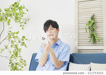 一個男人在客廳一邊思考一邊使用智慧型手機 111731015