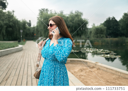 Young pretty woman model in stylish dresses talk by mobile cell phone look aside standing on summer in spring park outdoors 111733751