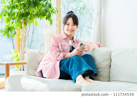 Young woman looking at her smartphone in the living room Young woman looking at her smartphone in the living room 111734539