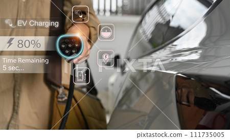 Businessman holding an electric vehicle charging gun connector standing in home garage Businessman holding an electric vehicle charging gun connector standing in home garage 111735005