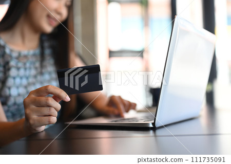 Select focus on businesswoman hand holding credit card and using laptop on wooden table Select focus on businesswoman hand holding credit card and using laptop on wooden table 111735091