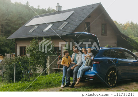 Family with electric car standing in front their house with solar panels on roof. Solar energy and sustainable lifestyle of young family. Concept of green energy and sustainable future for next Family with electric car standing in front their house with solar panels on roof. Solar energy and sustainable lifestyle of young family. Concept of green energy and sustainable future for next 111735215