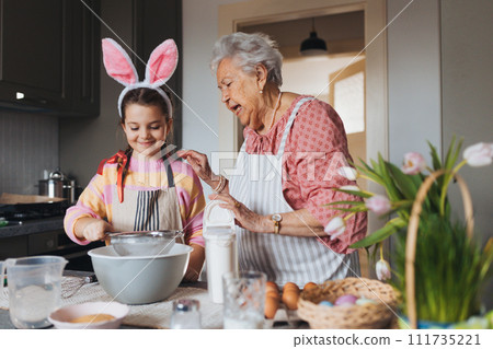 Grandmother with grandaughter preparing traditional easter meals, baking cakes and sweets. Passing down family recipes, custom and stories. Grandmother with grandaughter preparing traditional easter meals, baking cakes and sweets. Passing down family recipes, custom and stories. 111735221
