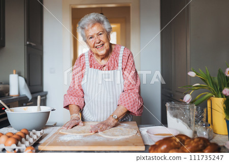 Senior woman preparing traditional easter meals for family, kneading dough for easter cross buns. Recreating family recipes, custom. 111735247