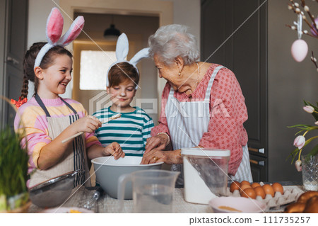 Grandmother with grandchildren preparing traditional easter meals, baking cakes and sweets. Passing down family recipes, custom and stories. 111735257