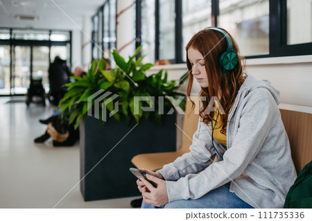Teenage girl waiting in hospital corridor, listening music. Adolescent patient coming to hospital for examination. 111735336