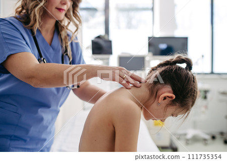Orthopedist examines the spine, posture, and spinal deformities of little girl. Girl visiting paediatrician for annual preventive exam. Concept of preventive health care for children. 111735354