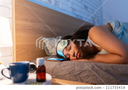 Woman sleeping with sleep mask, using sleeping pills, melatonin. Concept of sleep routine. Insomnia a sleep problems among adults. 111735419