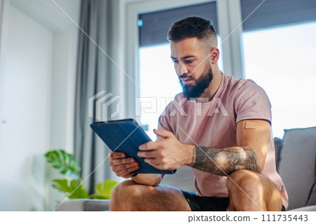 Young man with nicotine patch on his shoulder, holding tablet. New Year's resolutions, quitting smoking, healthy lifestyle without cigarettes. 111735443