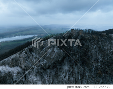 Aerial view of old ruins of fortress in the middle of winter forest. Drone view of snowy landscape with broken stone walls. 111735479