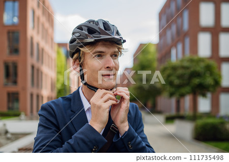 Handsome middle-aged man commuting through the city by bike in suit. Male city commuter traveling from work by bike after a long workday. Handsome middle-aged man commuting through the city by bike in suit. Male city commuter traveling from work by bike after a long workday. 111735498
