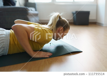 Woman exercising at home, stretching her body. Solo home workout and meditation, morning or evening workout routine. 111735514
