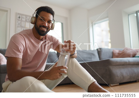 Young man resting after home workout and meditation, morning or evening workout routine, listening to music through wireless headphones. 111735555