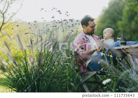 Low angle shot of man working outdoors in the garden, eating lunch, sandwich. Businessman working remotely from homeoffice, thinking about new business or creative idea. Low angle shot of man working outdoors in the garden, eating lunch, sandwich. Businessman working remotely from homeoffice, thinking about new business or creative idea. 111735643