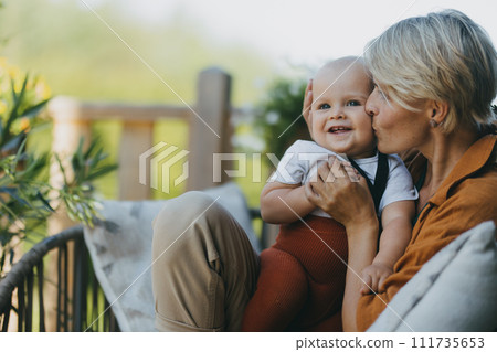 Beatiful mother sitting with little son outdoors, in garden patio. Warm spring day of mother with toddler. Hygge motherhood. 111735653