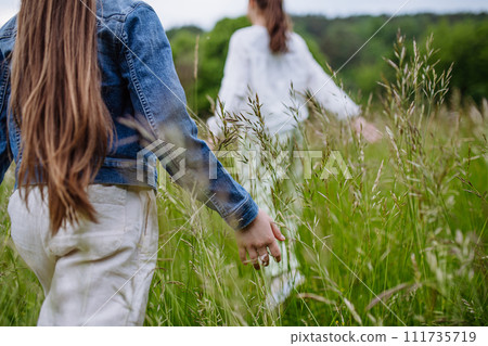 Two sisters playing at meadow in grass, having fun, running a laughing. Sisterly love and siblings relationship concept. Two sisters playing at meadow in grass, having fun, running a laughing. Sisterly love and siblings relationship concept. 111735719