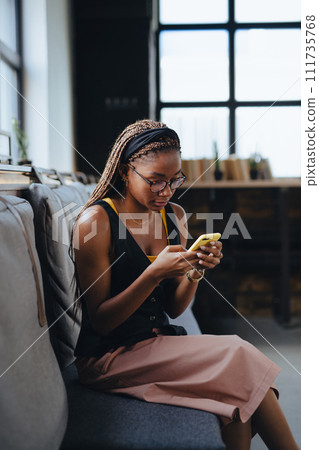 Portrait of beautiful woman sitting in modern office looking at smartphone, taking break. Working remotely from coffee shop. Portrait of beautiful woman sitting in modern office looking at smartphone, taking break. Working remotely from coffee shop. 111735768
