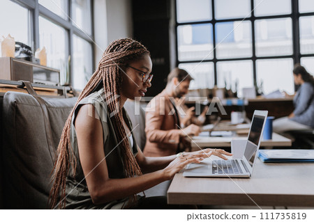 Beautiful businesswoman working on laptop in modern office. Group of freelancers working in shared work area. Concept of coworking, common workspaces for business, startups. Beautiful businesswoman working on laptop in modern office. Group of freelancers working in shared work area. Concept of coworking, common workspaces for business, startups. 111735819