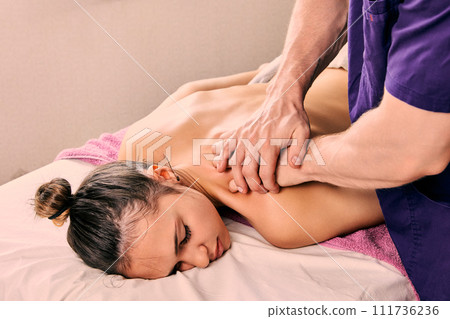 Spa beauty salon, massage therapist gives back massage to young woman in his 20s lying on massage table. Spa beauty salon, massage therapist gives back massage to young woman in his 20s lying on massage table. 111736236