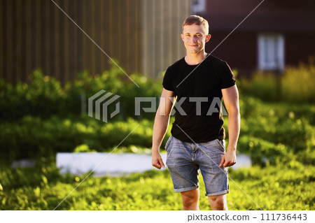 Horizontal knee length portrait of white man in her 20s, Caucasian male standing in garden at sunset Horizontal knee length portrait of white man in her 20s, Caucasian male standing in garden at sunset 111736443