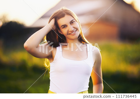 Perfect teeth of young Caucasian woman with perfect smile at setting sun against blurred background of rural landscape. 111736445