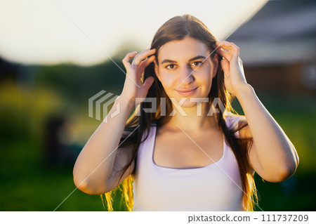 Street portrait of young Caucasian woman in light of setting sun in countryside, close-up. Street portrait of young Caucasian woman in light of setting sun in countryside, close-up. 111737209