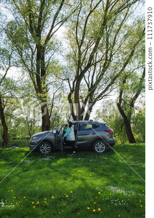 a woman gets into a parked car on a green lawn in nature 111737910