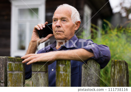 Senior man leaning on fence and talking on phone 111738116