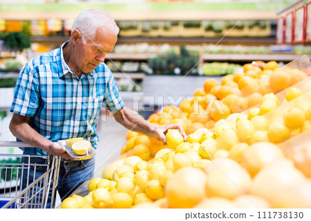 Mature senor examines oranges in fruit section of supermarket 111738130