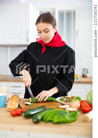 Female cook in black uniform chopping vegetables in kitchen 111738141