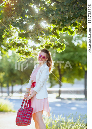 smiling elegant female in pink dress and white jacket in city 111738308