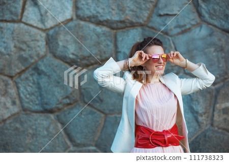 smiling elegant woman in pink dress and white jacket in city 111738323