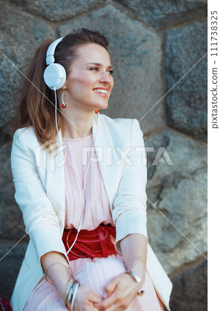 happy woman in dress and jacket in city listening to music 111738325