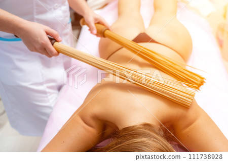 Woman masseuse doing double samurai massage with bamboo brooms in spa. Relaxing massage concept 111738928