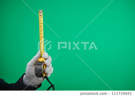 Close up view of Worker Man Hand with Tape Measure. Male Hand wearing Working cotton Glove with Tape-measure. Human hand holding tape measure. advertising Green background chromakey copy space 111738941