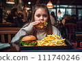 Fat girl eating hamburger in fast food restaurant.  111740246