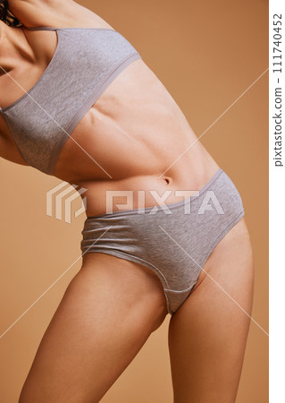 Cropped portrait of flexible woman doing exercises in grey underwear against sandy color studio background. Yoga and recreation. 111740452