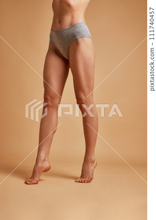 Cropped portrait of slim and smooth female legs against sandy color studio background. Model posing in lingerie. Concept of beauty treatment. Cropped portrait of slim and smooth female legs against sandy color studio background. Model posing in lingerie. Concept of beauty treatment. 111740457
