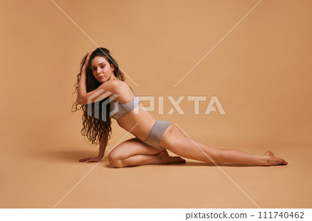 Portrait of young beautiful slim woman in lingerie posing against sandy color studio background. Model in grey underwear. Portrait of young beautiful slim woman in lingerie posing against sandy color studio background. Model in grey underwear. 111740462
