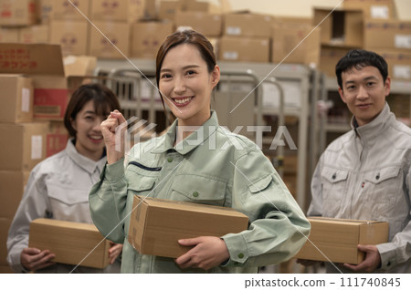 Three men and women in work clothes working in a distribution warehouse Three men and women in work clothes working in a distribution warehouse 111740845