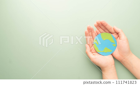 World Earth Day. Human hands holding globe symbol on green background. Concept of green energy, ESG, renewable, sustainable resources and environmental care. Flat layout. 111741823