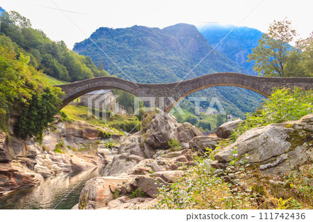 Ancient double arch stone Roman bridge (Ponte dei Salti) over the clear water of the Verzasca river in Lavertezzo ,Verzasca Valley, Ticino Canton, Switzerland 111742436
